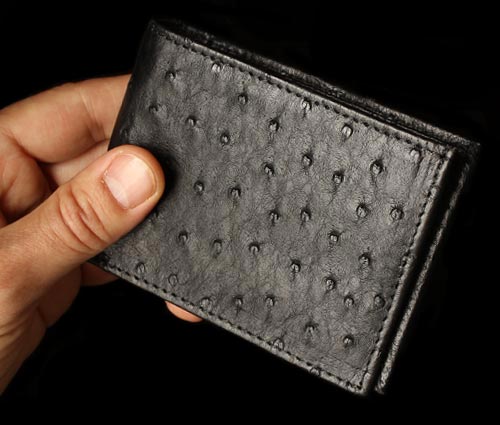 A closeup view of a man's hand holding a black ostrich leather wallet.