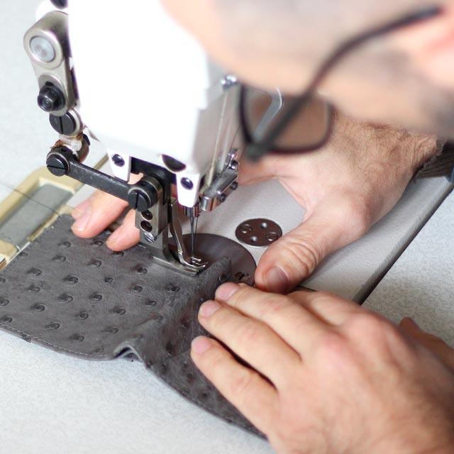 A closeup view of a man busy using a industrial sewing machine to make a ostrich wallet.